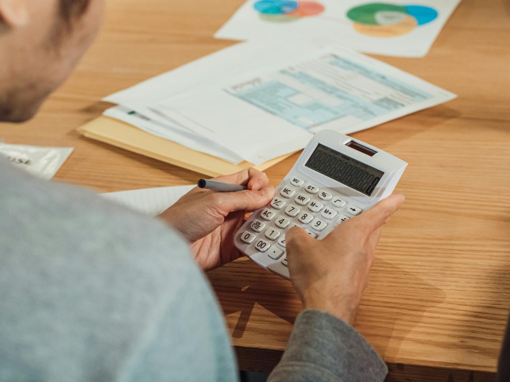 Pessoa usando calculadora para revisar orçamento com papéis e gráficos sobre a mesa