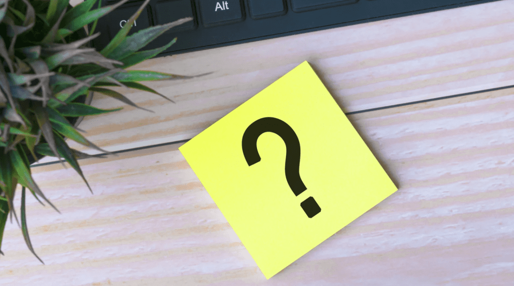 Post-it amarelo com ponto de interrogação sobre mesa de madeira, simbolizando dúvidas que, se não forem solucionadas, podem causar atraso de obra.