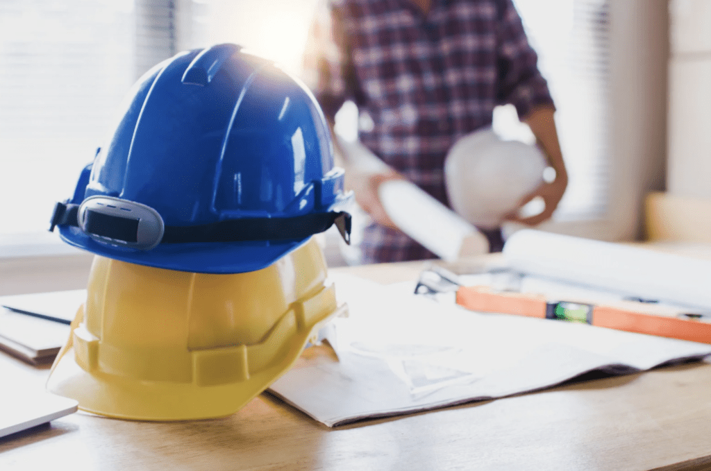 Capacetes de obra sobre mesa com projetos, reforçando a importância do planejamento para obra sem retrabalho.