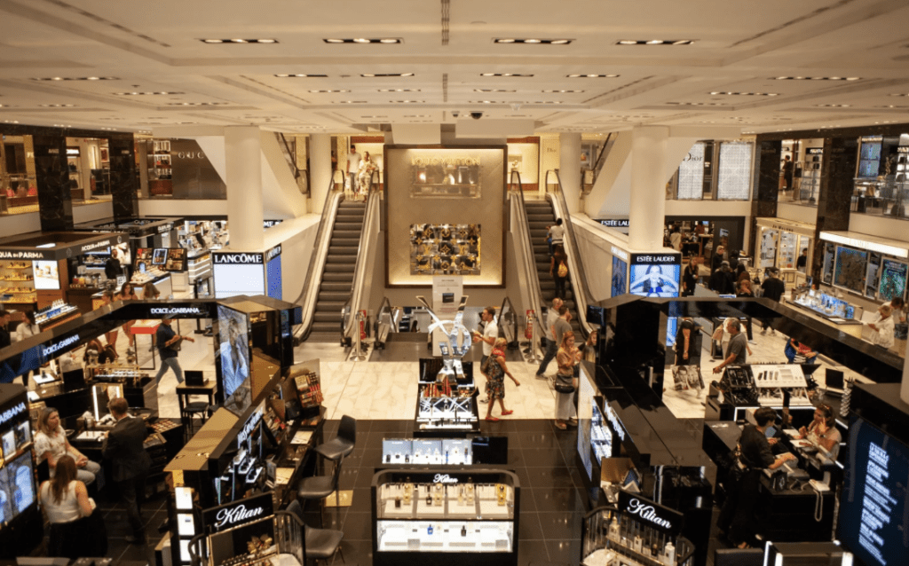 Vista interna de um shopping com diversas lojas e escadas rolantes, ilustrando a importância das obras comerciais em shoppings para padronização e experiência do consumidor.