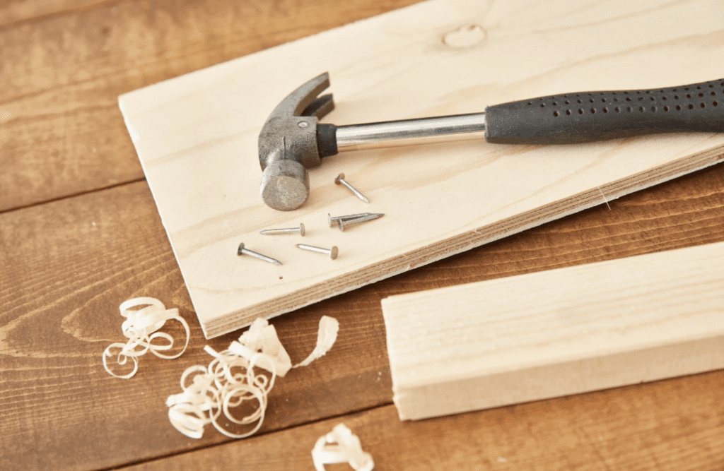 Martelo, pregos e tábua representando o início da marcenaria em obra.